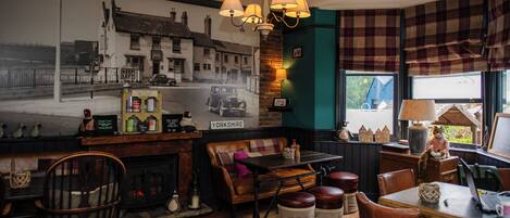 A cozy pub interior with a vintage car mural, wooden furniture, and a fireplace.