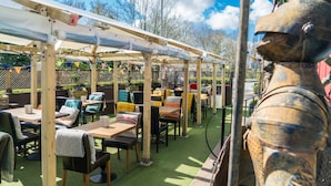 An outdoor patio with wooden tables and chairs, a covered seating area, and a statue. - Grantham Arms (York)