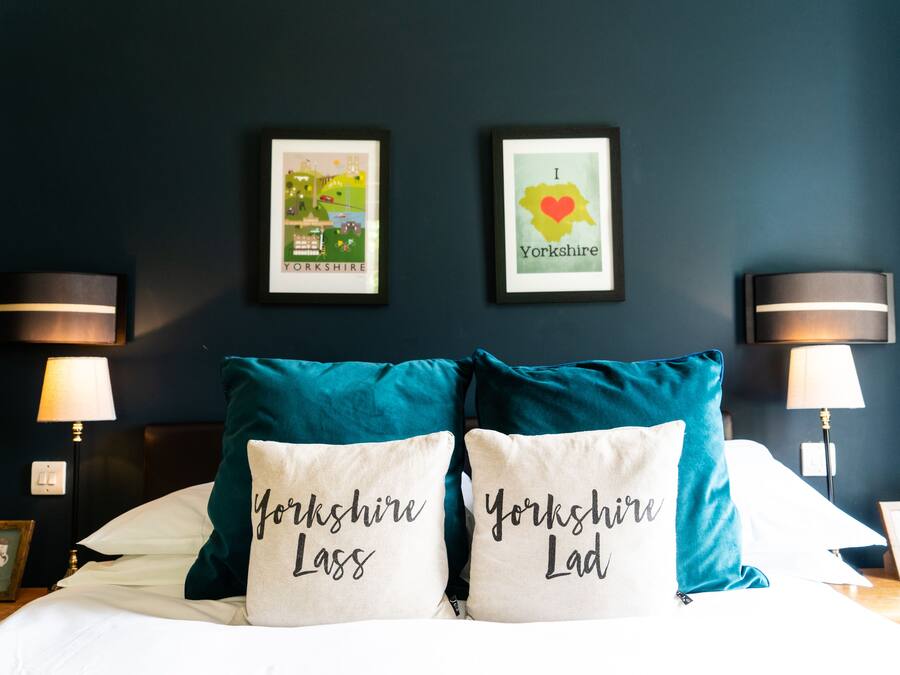 Habitación de hotel con una cama, dos cuadros en la pared, dos lámparas y dos almohadas con el texto 'Yorkshire Lass' y 'Yorkshire Lad'.