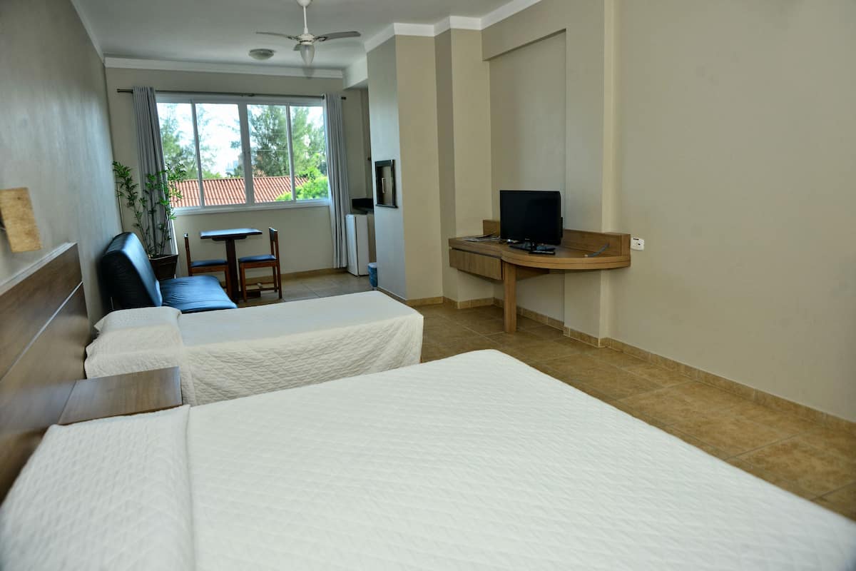 A hotel room with two beds, a desk, a chair, a ceiling fan, and a window with curtains.