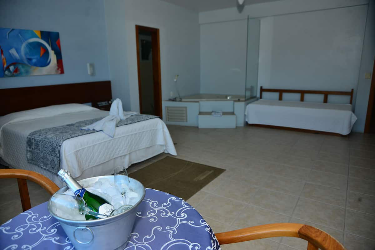 A hotel room with a bed, a small table with a bottle of champagne, a chair, and a large mirror.