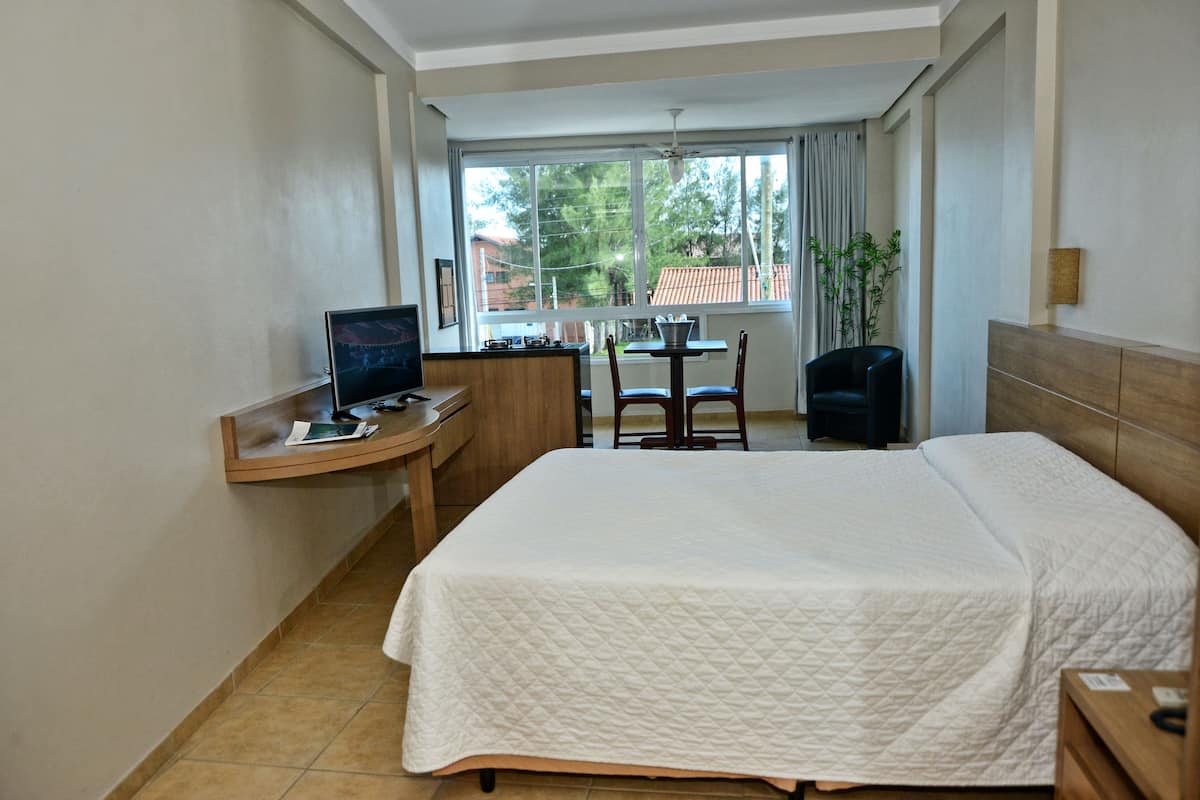 A hotel room with a bed, a desk with a computer, a chair, and a view of the outside.
