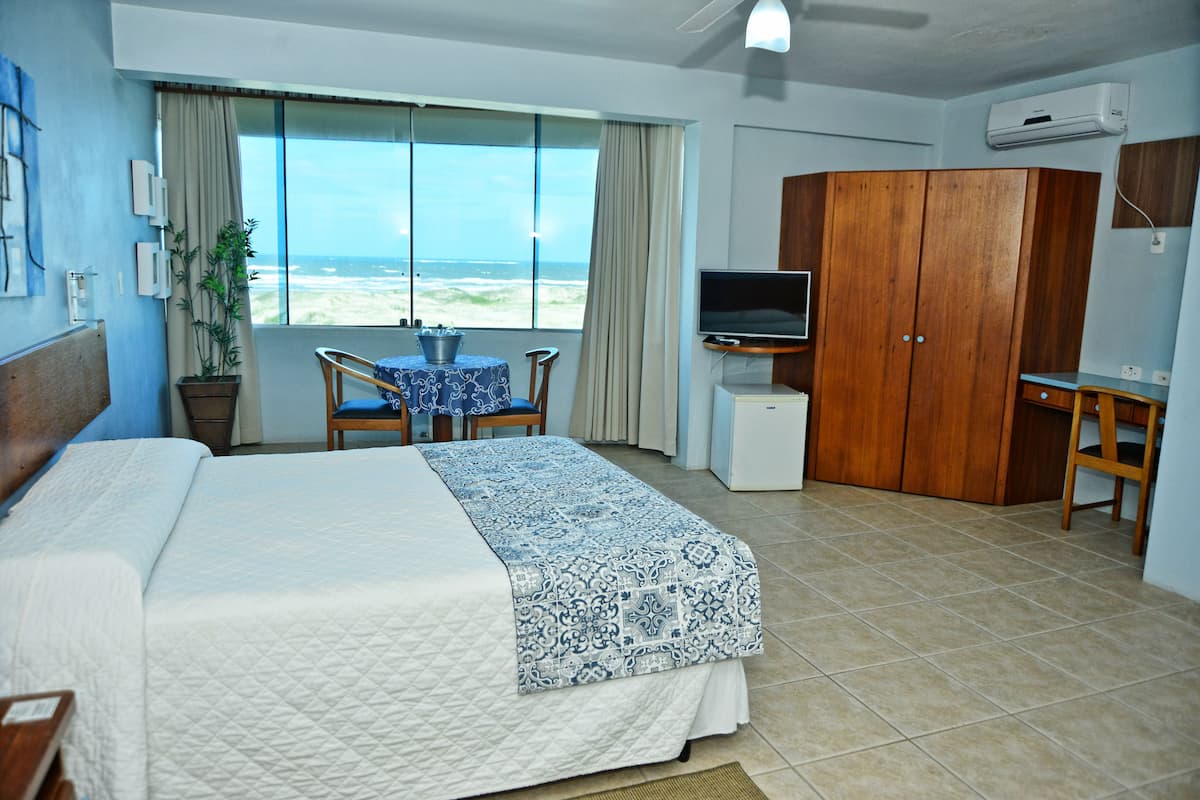 A hotel room with a bed, a desk, a television, and a view of the ocean.