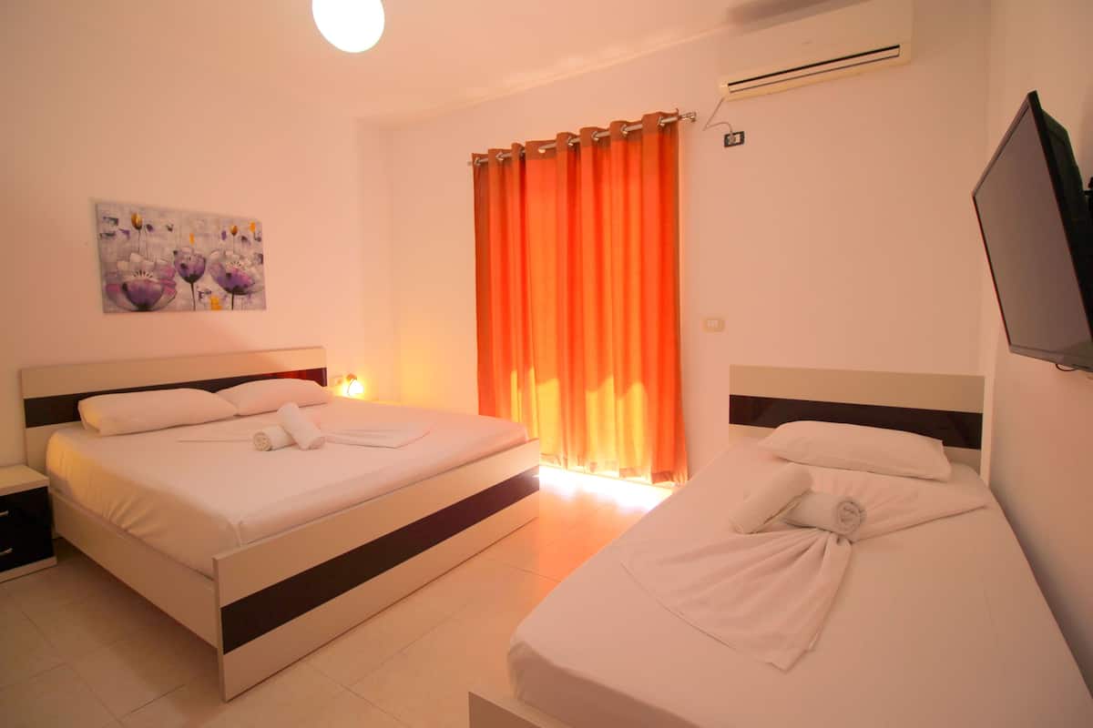 A hotel room with two beds, a painting on the wall, an air conditioner, and a TV mounted on the wall.