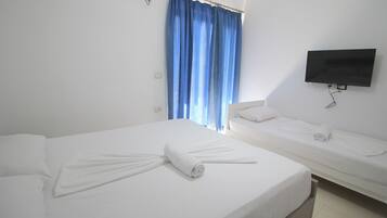 A hotel room with two beds, a TV mounted on the wall, and a window with blue curtains.