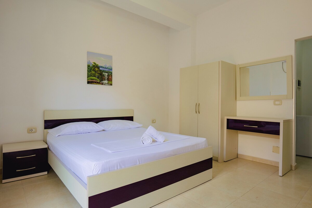 A bedroom with a bed, a nightstand, a wardrobe, and a desk with a mirror.