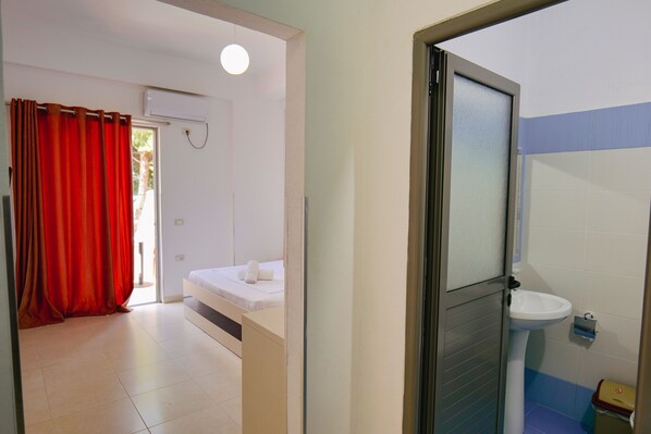 A hotel room with a bed, a bathroom with a sink, and a red curtain.