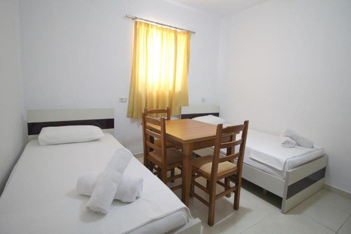 A small, clean room with two single beds, a wooden table, and a chair.