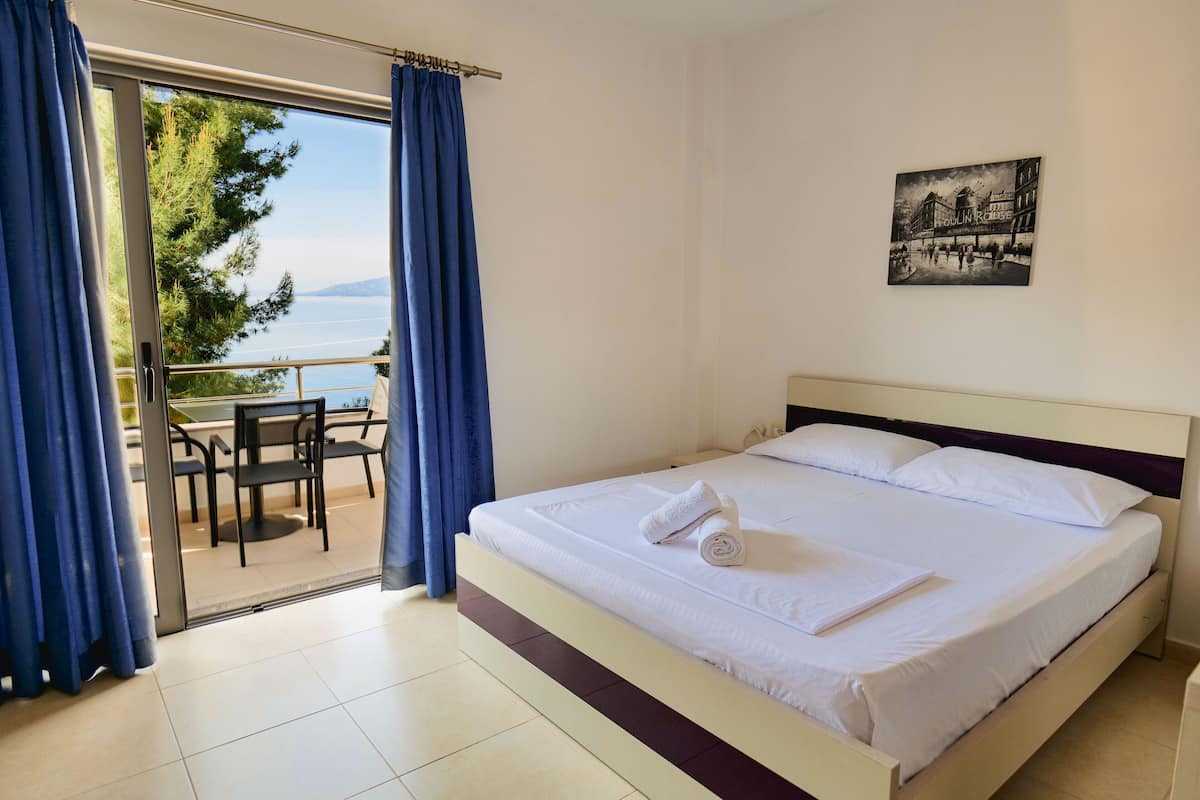A hotel room with a bed, a painting, and a view of a body of water through a glass door.