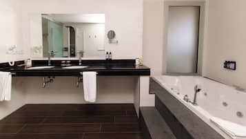 Un baño moderno con un espejo grande, dos lavamanos, una bañera y suelo de madera oscura.