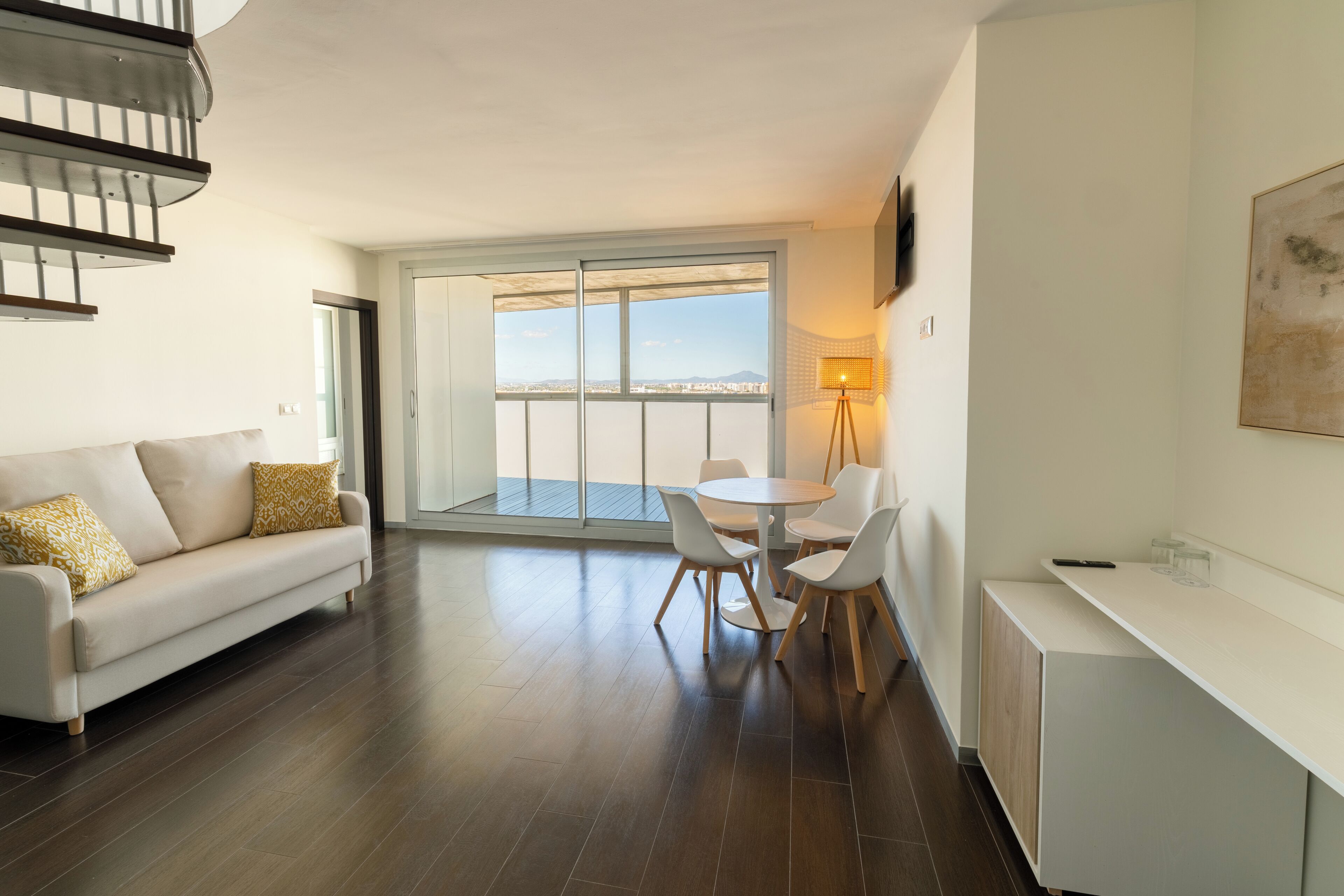 Uma sala de estar moderna com sofá, mesa de jantar, cadeiras, televisão e varanda com vista.