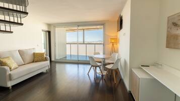 Uma sala de estar moderna com sofá, mesa de jantar, cadeiras, televisão e varanda com vista.