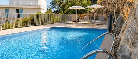Une piscine à l’eau d’un bleu cristallin, une échelle en métal, des chaises longues et des parasols.