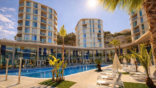 Un hotel con piscina, sillones de descanso y palmeras.