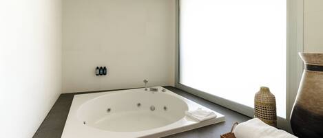 Un baño moderno con una bañera independiente, un ventanal con vistas y un pequeño estante con artículos de aseo.