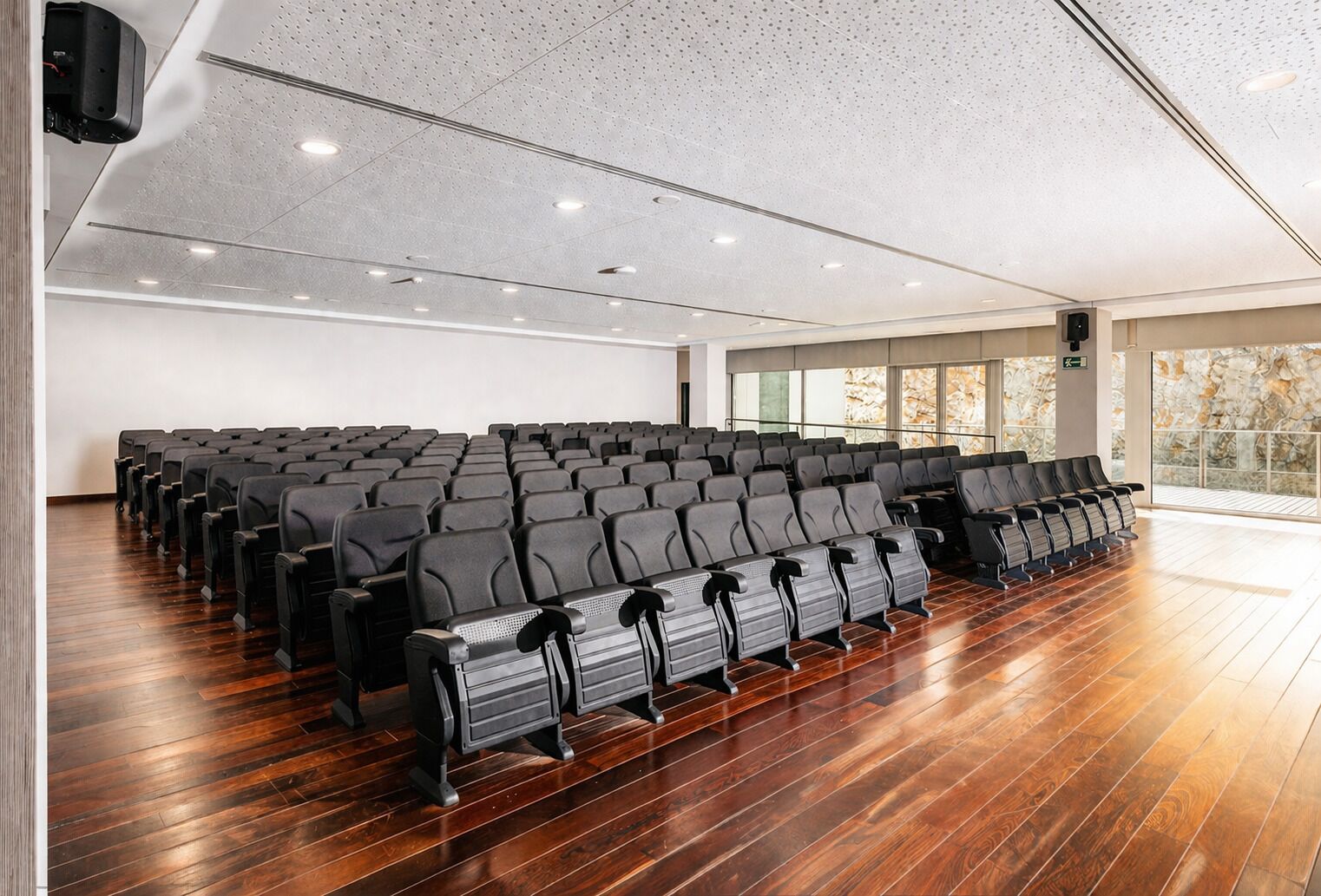 A conference room with rows of chairs, a wooden floor, and a ceiling with recessed lighting.