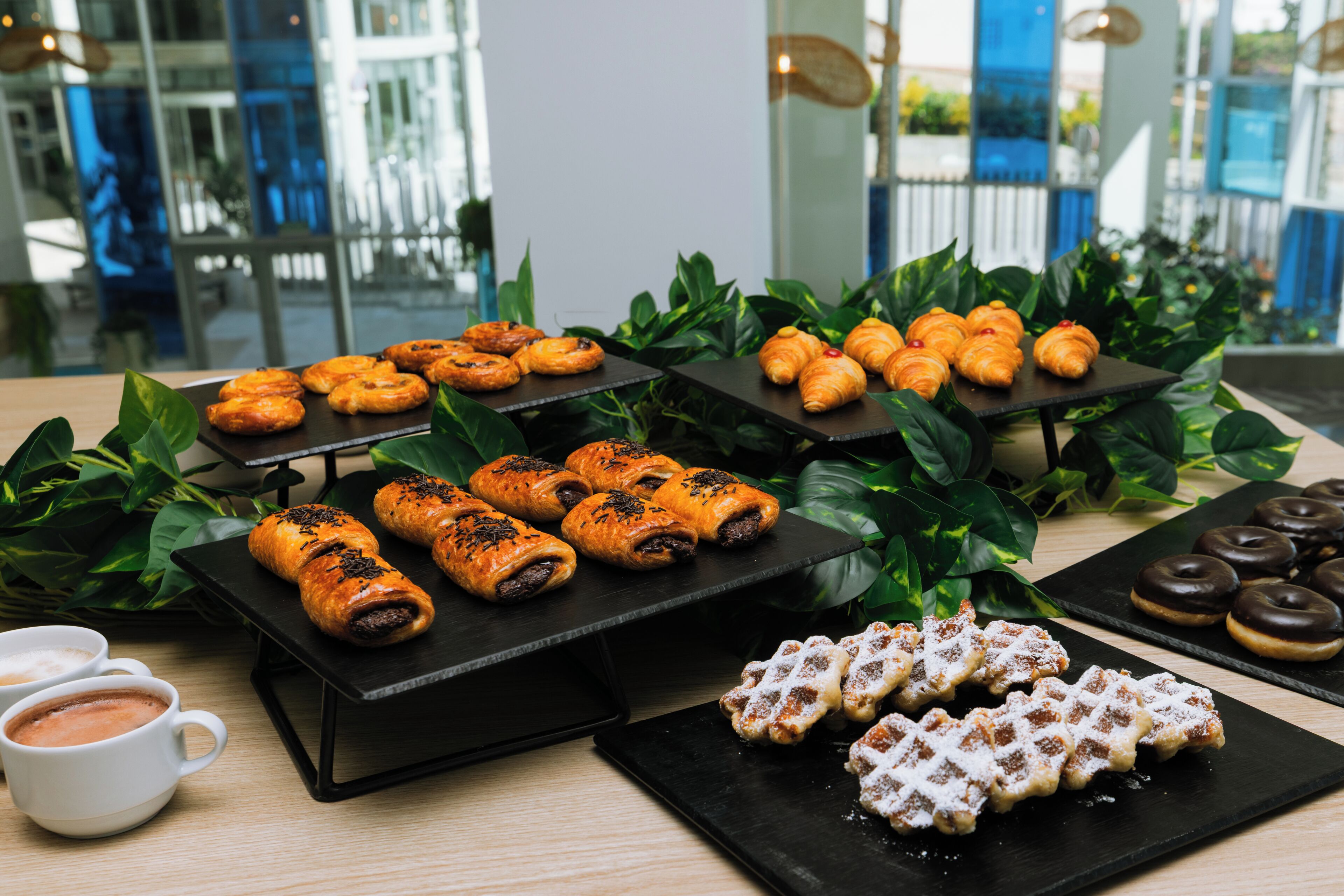 Diverse gebakjes en koffie op een tafel, omringd door groene planten.
