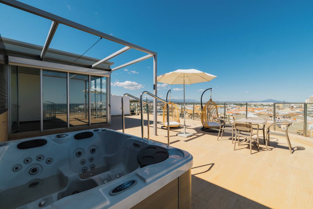 Una terraza en la azotea con jacuzzi, mobiliario exterior y vistas a la ciudad.