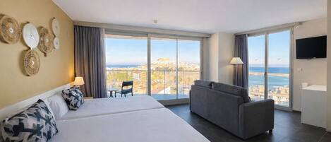 A hotel room with two beds, a sofa, a TV, and a balcony with a city view.