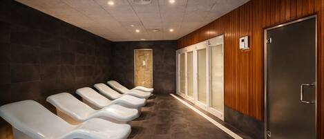A row of white massage chairs, a wooden wall, and a large metal door.