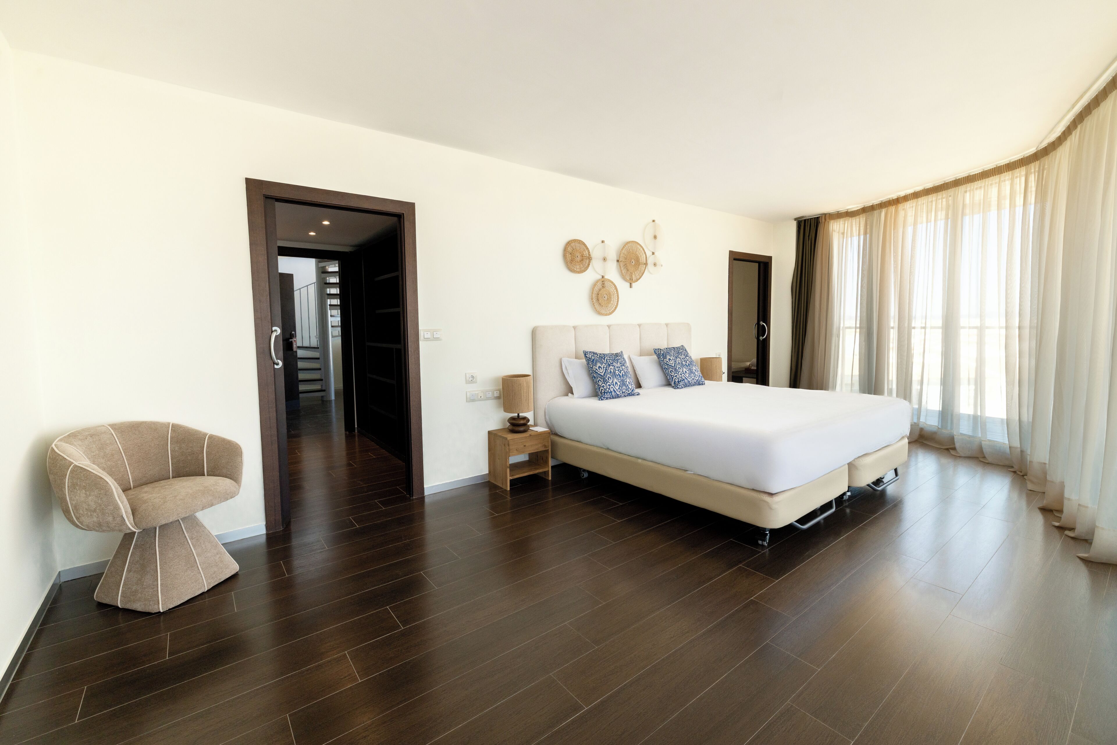A modern hotel room with a large bed, a chair, a nightstand, and a mirror.