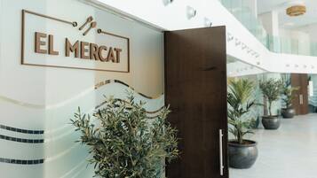Une entrée moderne, avec une enseigne indiquant « EL MERCAT » et des plantes en pot.