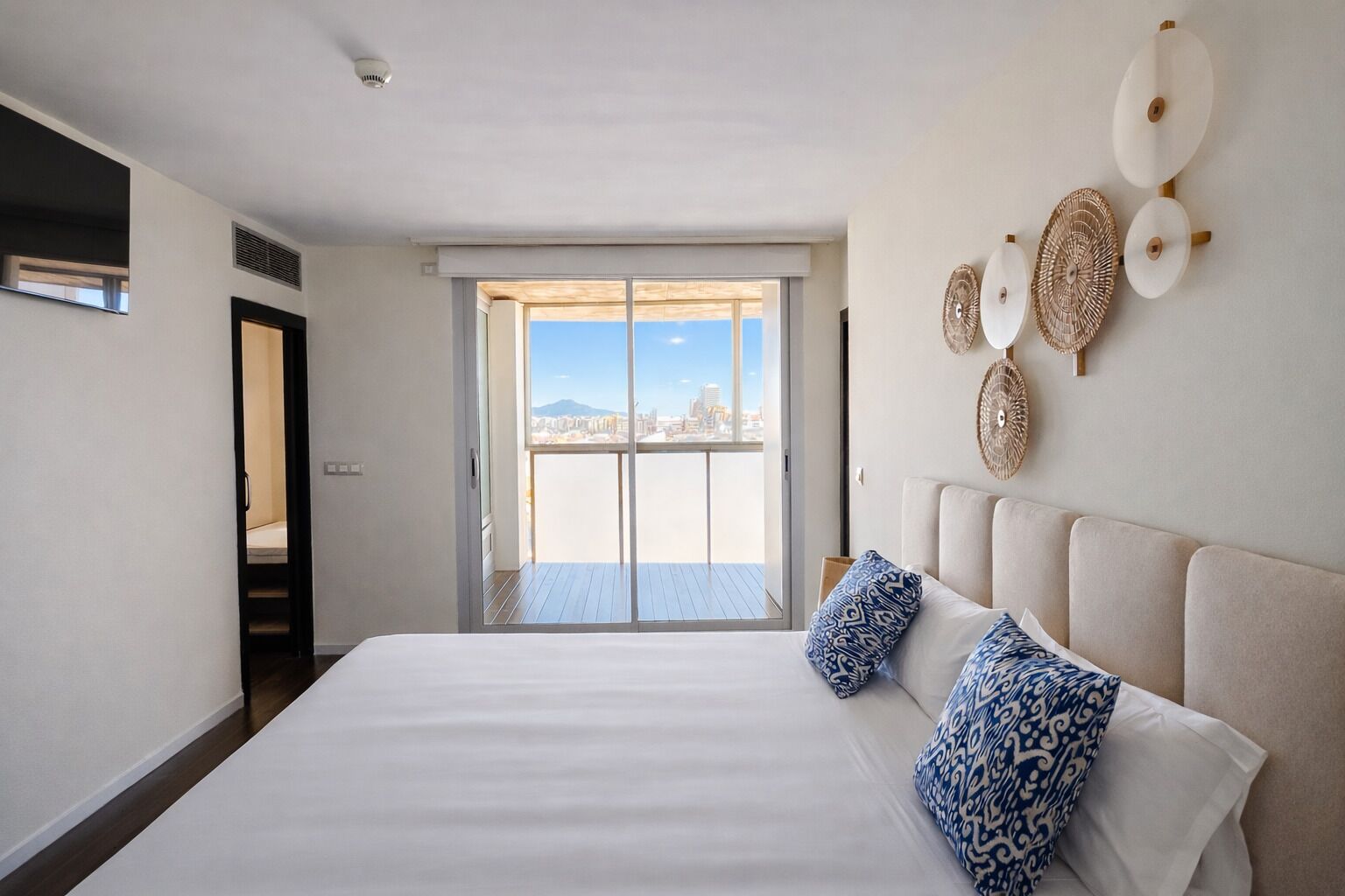 A hotel room with a large bed, a sliding door to a balcony, and a city view.