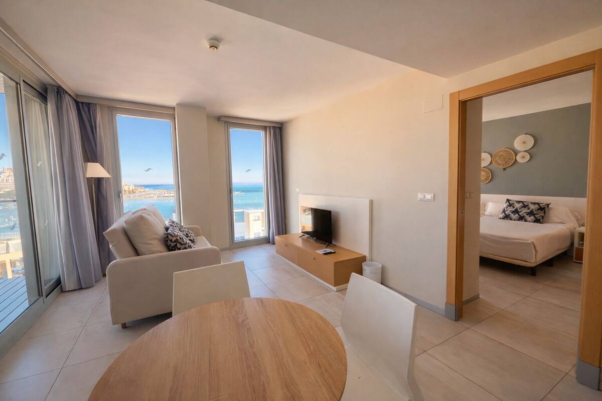 Una habitación de hotel moderna con balcón, televisión, zona de comedor y cama.