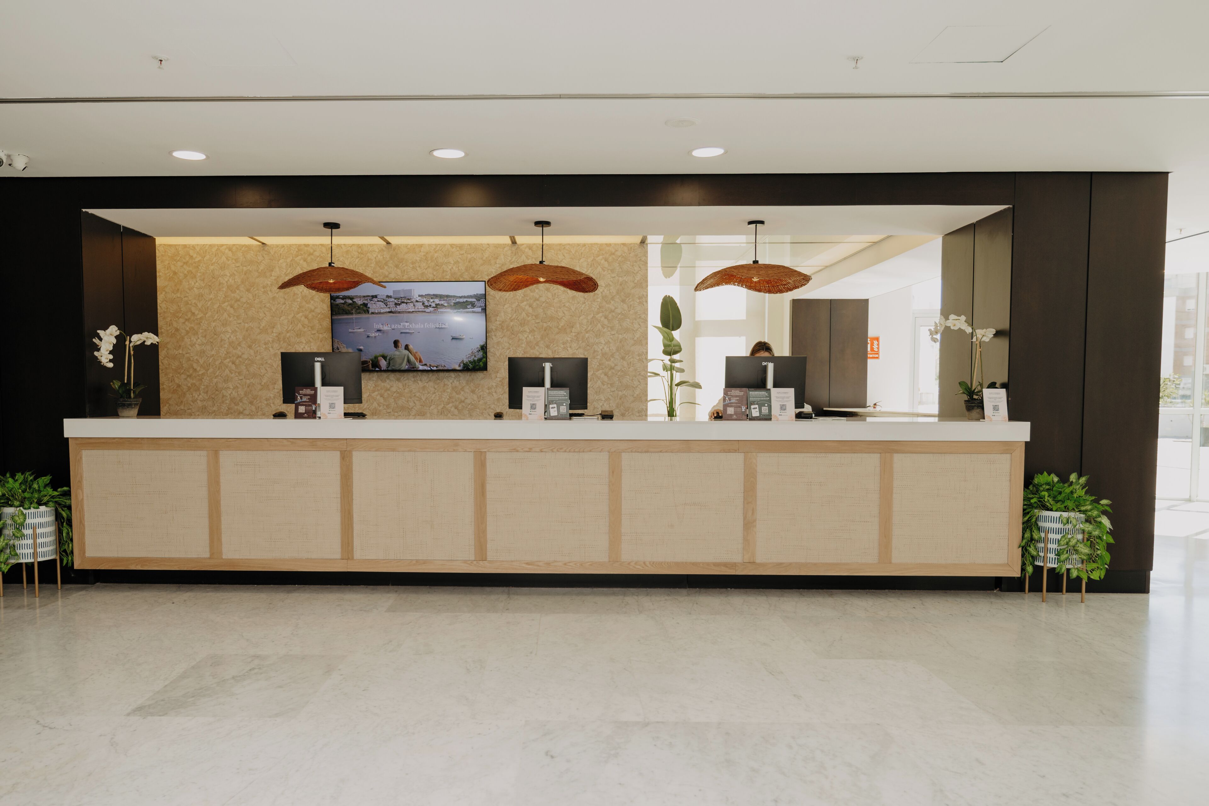 A reception desk with a flat-screen TV, two pendant lights, and a view of the sea.