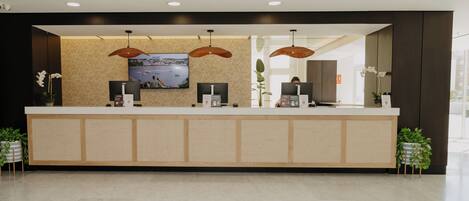 A reception desk with a flat-screen TV, two pendant lights, and a view of the sea.
