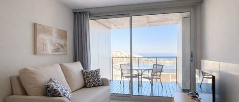 Una sala de estar moderna con un sofá, un televisor y un balcón con vistas al mar.