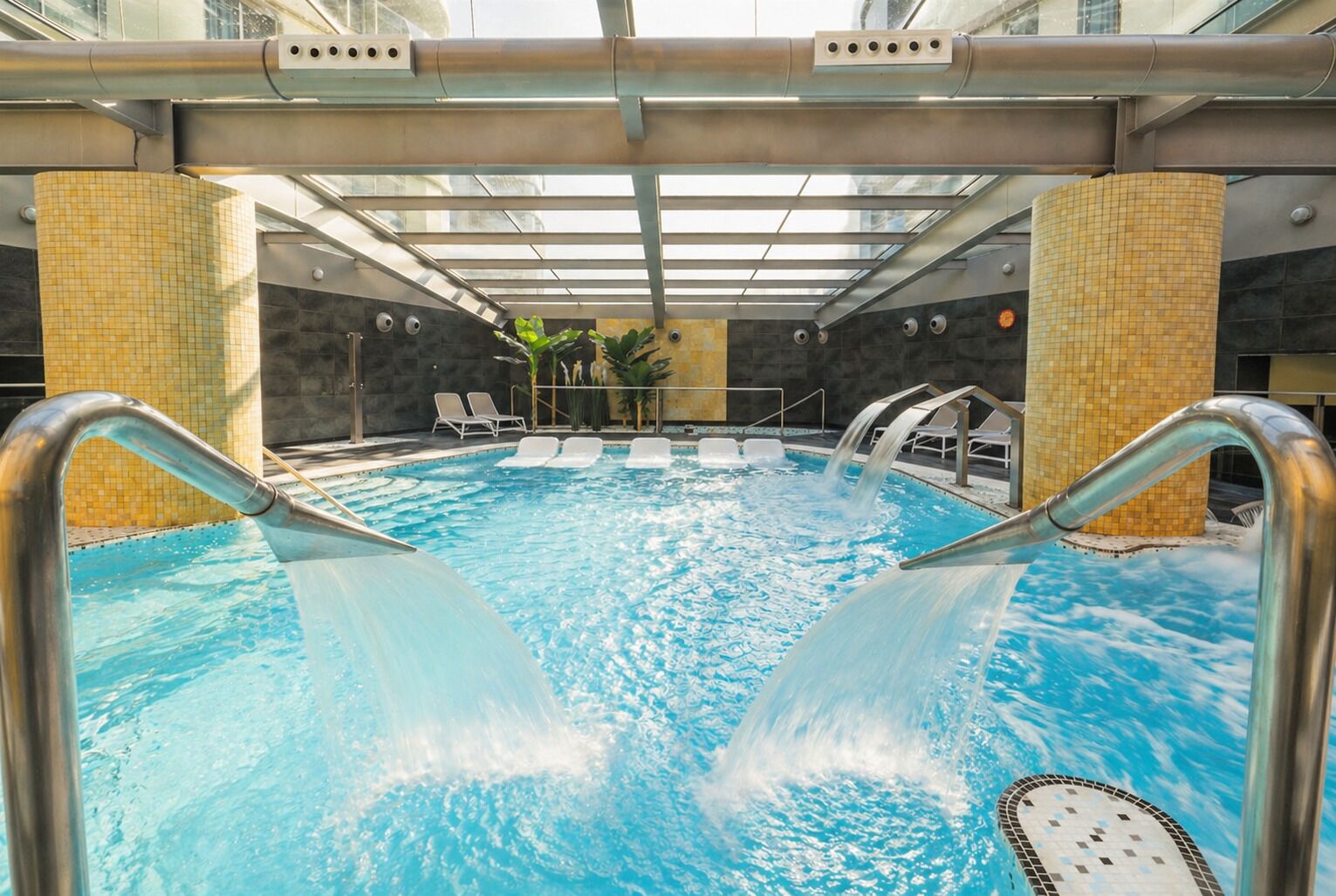 Ein Schwimmbecken mit Wasserrutsche, Liegestühlen und einer Glasüberdachung.