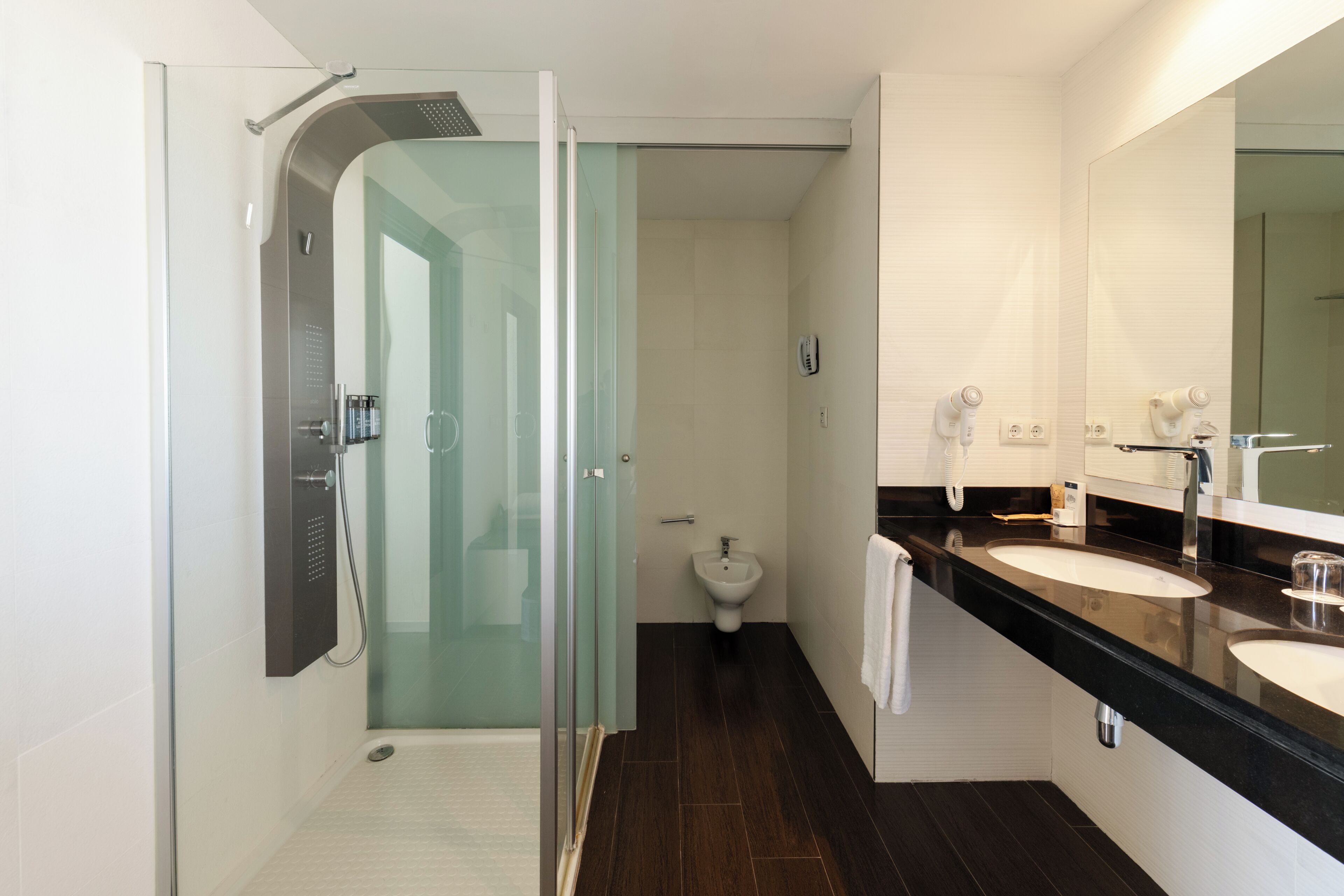 Une salle de bain moderne dotée d’une douche à parois de verre, d’un bidet et d’un meuble-lavabo à deux vasques.