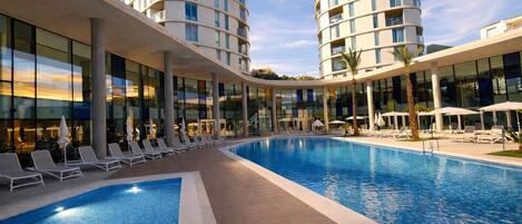 Un hôtel doté d’une grande piscine, de chaises longues et d’une architecture moderne.