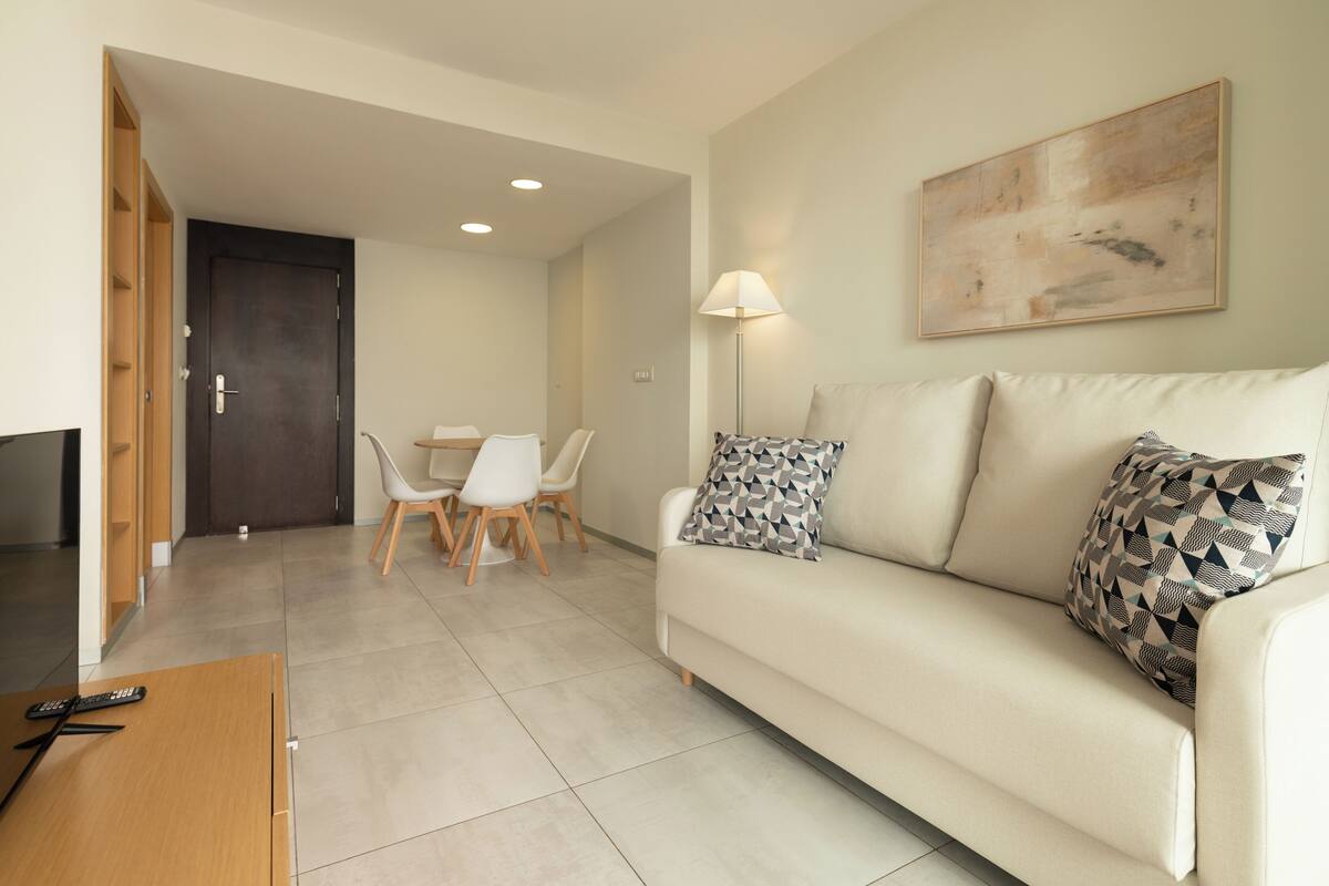 Una sala de estar moderna con un sofá, un televisor, una mesa de comedor con sillas y un cuadro en la pared.