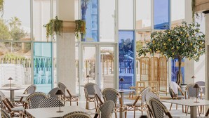 Amplio espacio interior con varias mesas y sillas, ventanas grandes y un árbol con frutos amarillos.