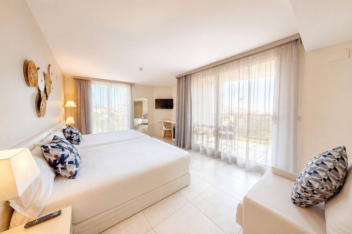 Habitación de hotel con una cama grande, un sofá, un televisor y un balcón con cortinas.