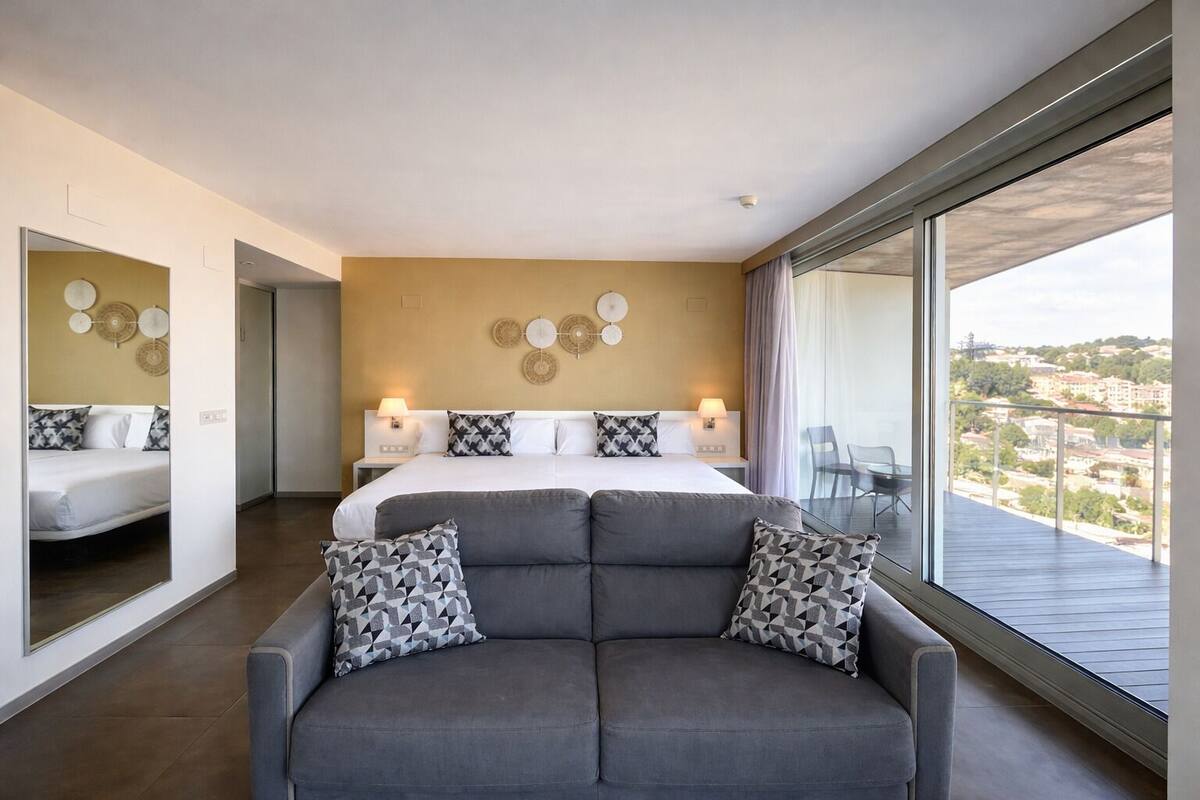 Una habitación de hotel moderna con una cama grande, un sofá y un balcón con vistas a la ciudad.