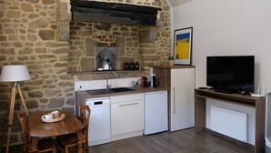 Une cuisine de taille réduite avec des murs en pierre, une table en bois, un téléviseur et une lampe.