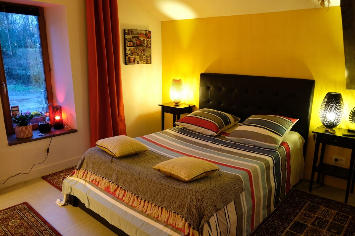 Een slaapkamer met een bed, twee bedlampen, een raam met gordijnen en een aan de muur bevestigd schilderij.