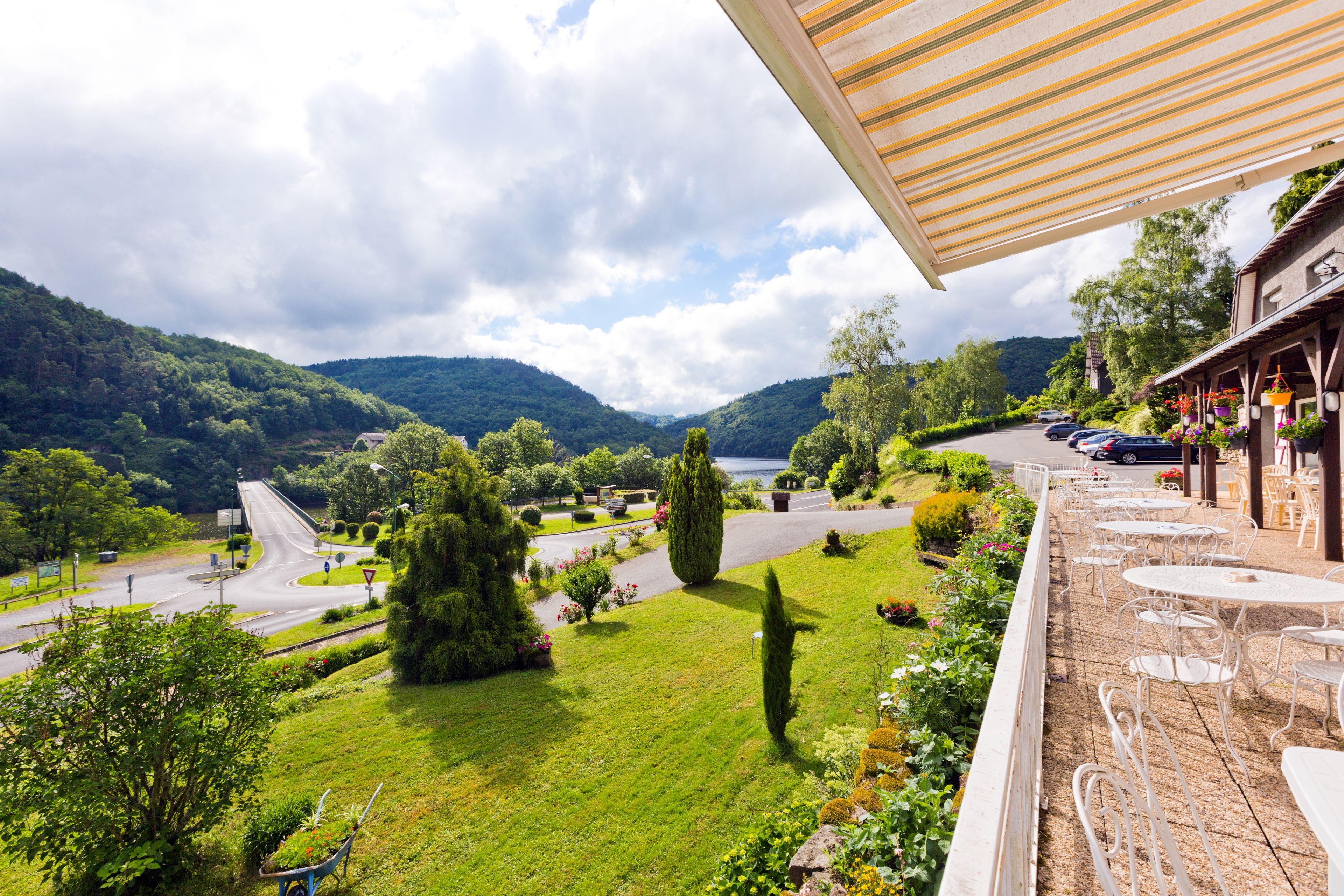 A hotel with outdoor seating, a view of a road, and surrounding greenery.