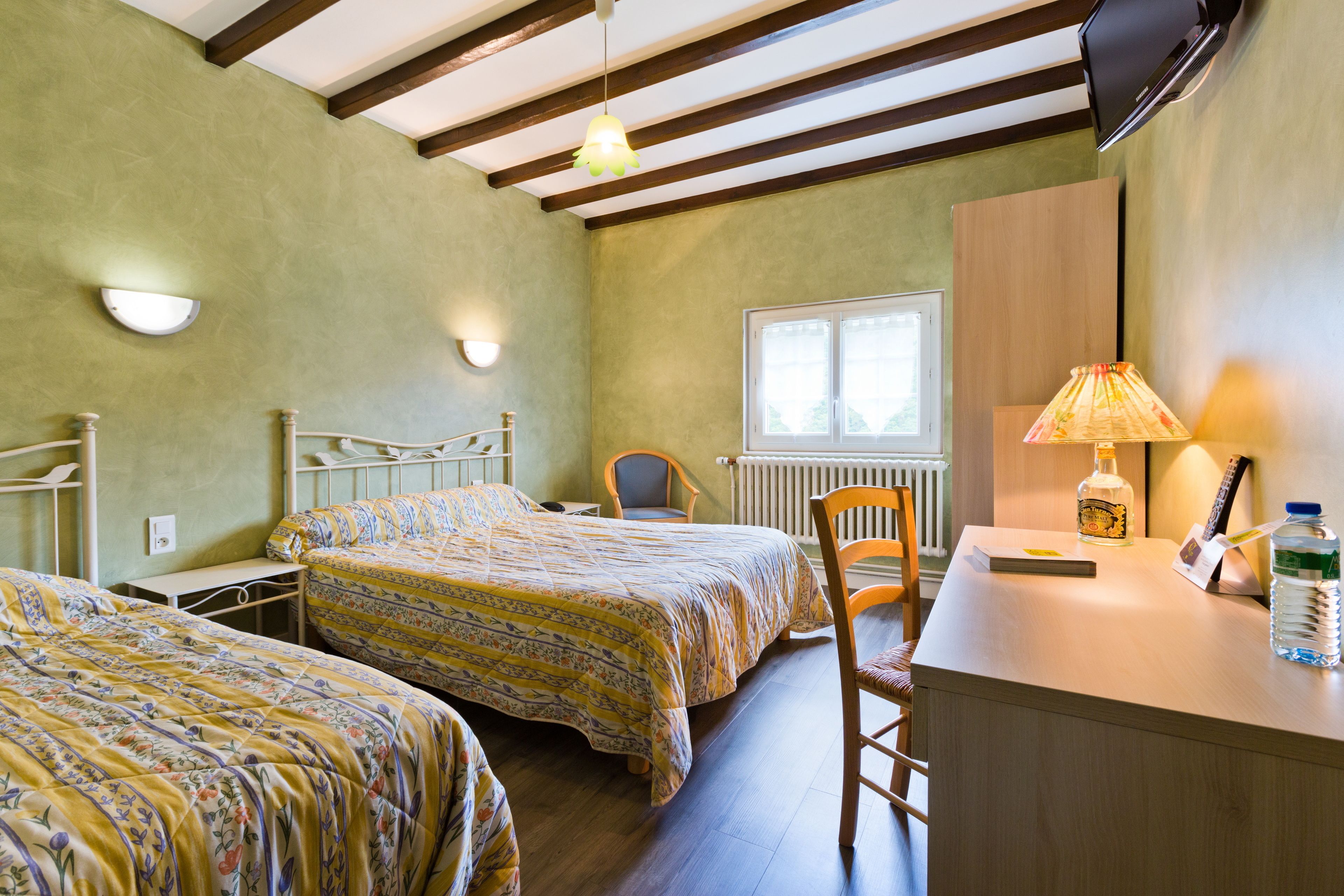 A room with two beds, a desk, a chair, a lamp, and a window.