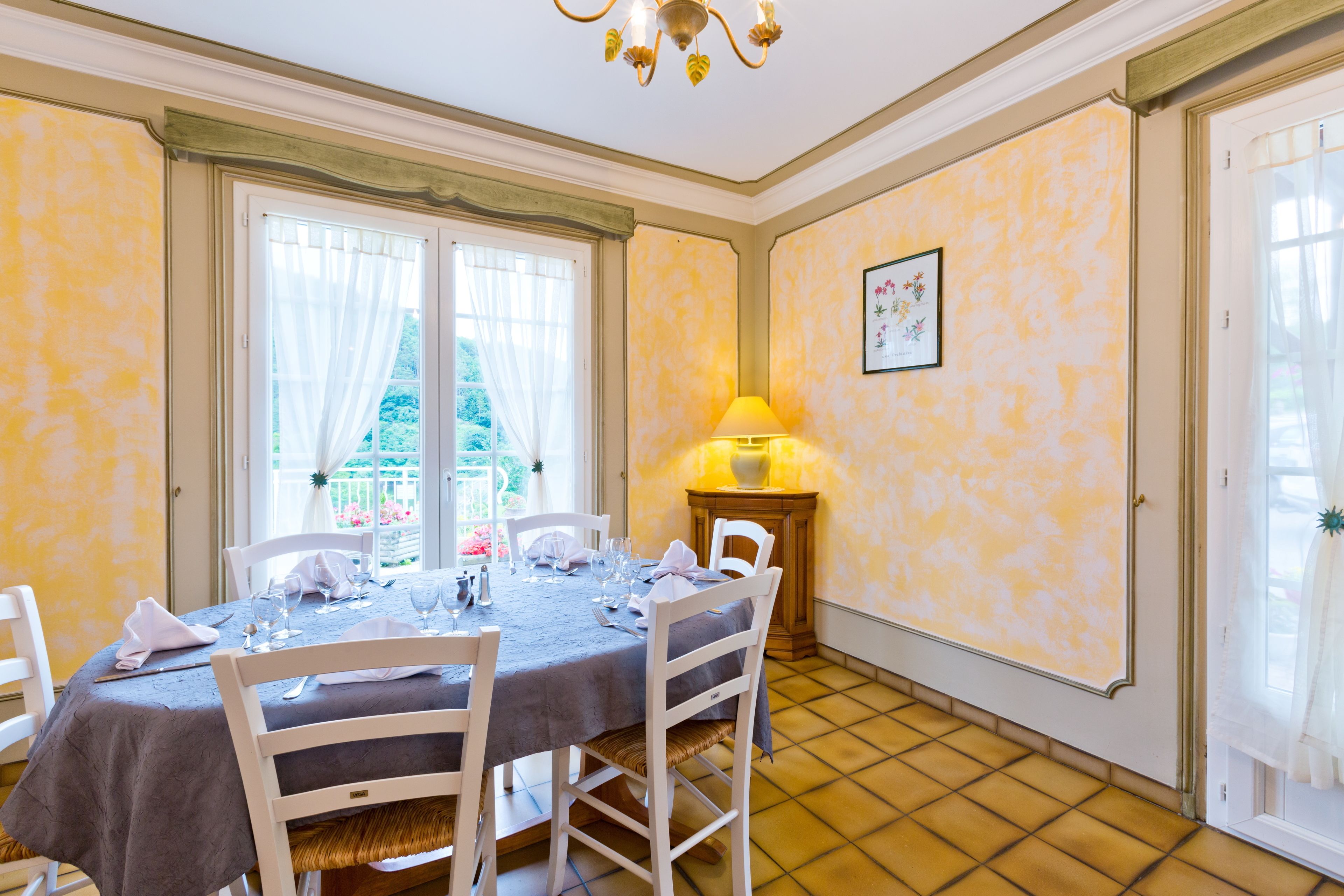 A dining room with a table set for four, white chairs, a chandelier, and a window with curtains.