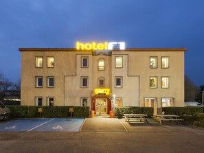 Un edificio de hotel con un letrero llamativo que dice 'hotel', un estacionamiento con acceso para discapacitados y una mesa de picnic.