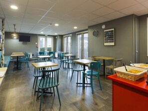 Un espace repas avec des tables et des chaises, une horloge au mur et un tableau encadré.