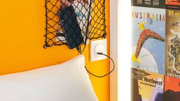 A wall with a yellow textured surface, a white pillow, a black netted area with a phone, and travel posters.