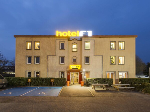 Un edificio de hotel con un cartel que dice 'hotel', un espacio de estacionamiento accesible para sillas de ruedas y una mesa de picnic.