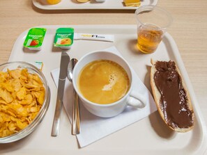 Una bandeja con una taza de café, un tazón de cereal, tostadas con crema de chocolate y dos pequeños recipientes de confitura.