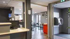 Un espace de bureau moderne comprenant un comptoir d’accueil, une machine à café et un coin repas avec des tables et des chaises.