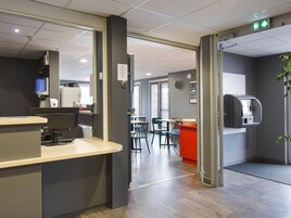 Un espacio de oficina moderno con mostrador de recepción, máquina de café y zona de comedor con mesas y sillas.